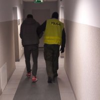 Policjant idzie z zatrzymanym mężczyzną korytarzem.