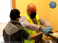 policjant zabezpiecza od zatrzymanego mężczyzny ślady daktyloskopijne robiąc odbitki odcisków palców na kartach daktyloskopijnych