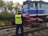 Policjant stojący obok volkswagena i pociągu osobowego uczestniczących w wypadku