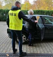 policjant w odblaskowej kamizelce z napisem na plecach policja trzyma drzwi samochodu do którego wsiada zatrzymana kobieta.