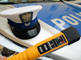 Czapka funkcjonariusza Wydziału Ruchu Drogowego leżąca na masce radiowozu na tle urządzenia służącego do pomiaru stężenia alkoholu w wydychanym powietrzu.