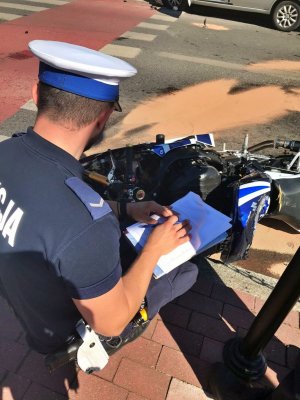 policjant w białej czapce przeprowadza klęczy przy rozbitym motocyklu