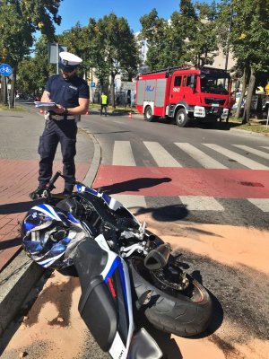 wóz strażacki w tle , policjant  przy rozbitym motocyklu