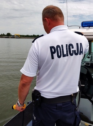 funkcjonariusz policji wodnej stoi na pokładzie łodzi z urządzeniem do pomiaru zawartości alkoholu w wydychanym powietrzu