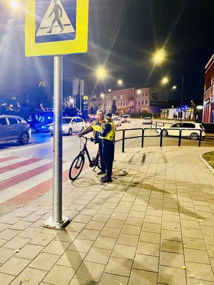 Przy przejściu dla pieszych policjantka wręcza rowerzyście kamizelkę odblaskową