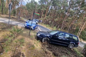 Policyjny radiowóz i auto typu kombi po za drogą, na terenie leśnym.