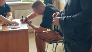 Zatrzymany mężczyzna z kajdankami na nadgarstkach podczas policyjnych czynności.