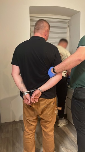 Zatrzymany mężczyzna z kajdankami na nadgarstkach podczas policyjnych czynności.