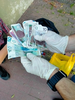 Dłonie mężczyzny w nylonowych rękawiczkach, który trzyma polskie banknoty.