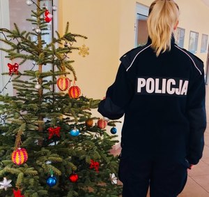 Umundurowana funkcjonariuszka Policji stojąca obok ubranego drzewka choinkowego.
