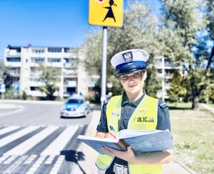 Policjanta z notatnikiem w ręku, w tle przejście dla pieszych.