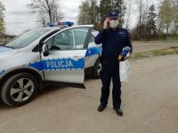 Umundurowany Policjant obok radiowozu z maskotką oraz torebka z prezentem