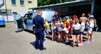 Dzieci stojące przy radiowozie i policjantach.