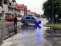 Policjant stojący na drodze przy radiowozie w deszczu.
