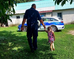 Dziecko idące za rękę z policjantem oraz radiowóz.