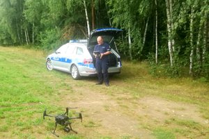 policjant w mundurze przy radiowozie i dron na ziemi, w oddali las