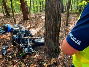 Rękaw koszuli policjanta z napisem policja i rozbity motocykl.