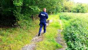 Policjant z psem tropiącym biegnie wzdłuż lasu.