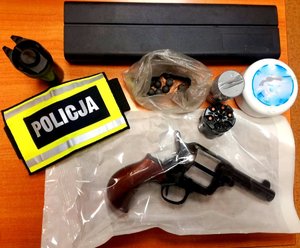 na biurku leży rewolwer, opakowanie na broń, w woreczku kule metalowe, opakowania na kule oraz opaska z napisem policja