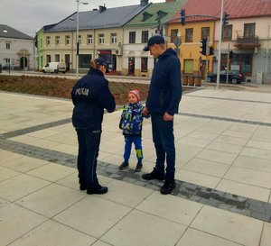 policjantka dająca opaskę odblaskową dziecku, które idzie z rodzicem za rękę