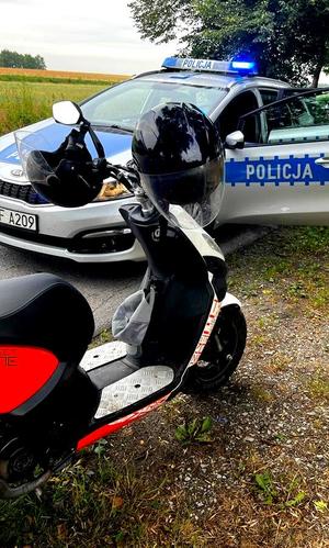 Radiowóz policyjny i motorower z dwoma kaskami zawieszonymi na kierownicy.