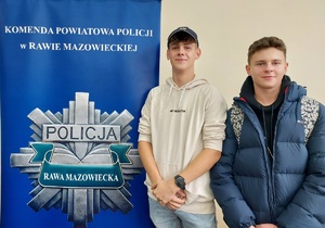 Dwóch chłopców, jeden w czapce policyjnej stoją obok plakatu o Policji.