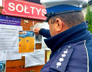 Policjant wiesza ulotkę na tablicy ogłoszeń.