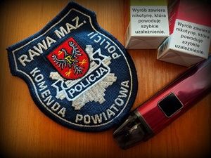 Naszywka na mundur z napisem Komenda Powiatowa Policji w Rawie Mazowieckiej, 2 opakowania zapasów do e-papierosa  z napisem wyrób zawiera nikotynę, która powoduje szybkie uzależnienie i e-papieros.