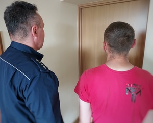 Policjant w mundurze stojący obok mężczyzny stojącego tyłem.