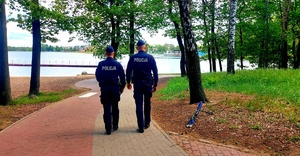 Policjanci idący ścieżką dla pieszych obok zalewu.