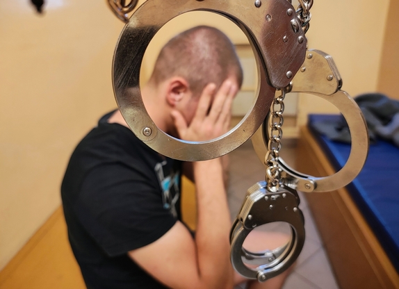 Kajdanki zespolone i mężczyzna zasłaniający dłońmi twarz.