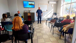 Policjant mówiący do grupy osób siedzących na krzesłach.