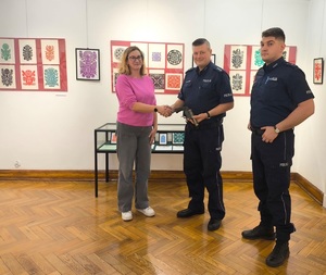 Dwóch policjantów jedne z nich przekazuje broń pracownikowi muzeum kobiecie.