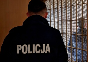 Policjant i zatrzymany stojący za kratami.