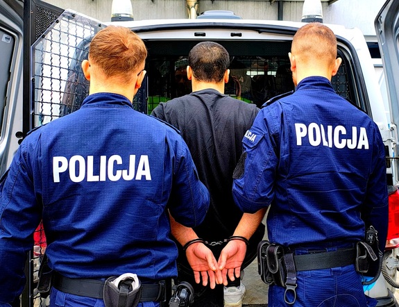 Dwaj policjanci i zatrzymany przy radiowozie.