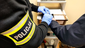Napis policja na opasce i w tle dłoń podczas robienia odcisków palców.
