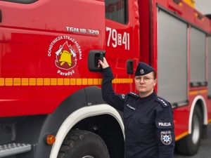 Policjantka trzymająca za klamkę drzwi radiowozu strażackiego.