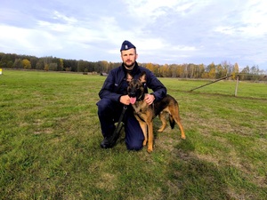 Policjant kucający przy psie.