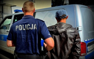 Policjant z zatrzymanym na tle radiowozu.