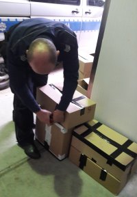 Policjant przenoszący pudełka z perfumami po wykonaniu oględzin i spisu do radiowozu