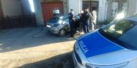 na pierwszym planie oznakowany radiowóz, dalej srebrny peugeot a przy nim dwaj policjanci i dwóch cywili