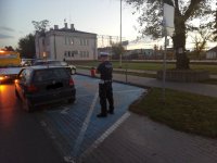 umundurowany policjant w białej czapce  stoi obok zaparkowanego na miejscu dla niepełnosprawnych vw , który za chwile będzie wciagany na widoczną przed nim lawetę