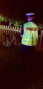 policjant w białej czapce i kamizelce odblaskowej stoi w nocy przy drodze, widać rower