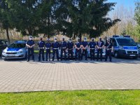 grupa umundurowanych policjantów stojących pomiędzy dwoma radiowozami