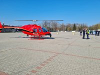 czerwony policyjni śmigłowiec stojący na placu, obok policjanci