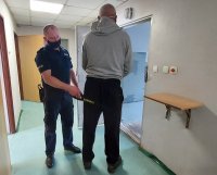 Policjant umieszcza w policyjnej celi zatrzymanego mężczyznę