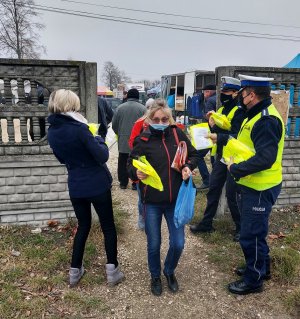 Policjanci wraz z pracownikiem Starostwa Powiatowego w Radomsku wręczają kamizelki odblaskowe w rejonie placu targowego w Przedborzu.