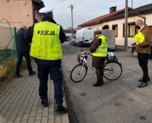 Policjanci wraz z pracownikiem Starostwa Powiatowego w Radomsku wręczają kamizelki odblaskowe w rejonie placu targowego w Kamieńsku