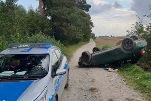 droga polna, stojący oznakowany radiowóz policyjny, leżący na dachu samochód audi