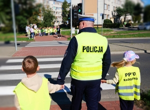 Policjant z dziećmi na przejściu dla pieszych.